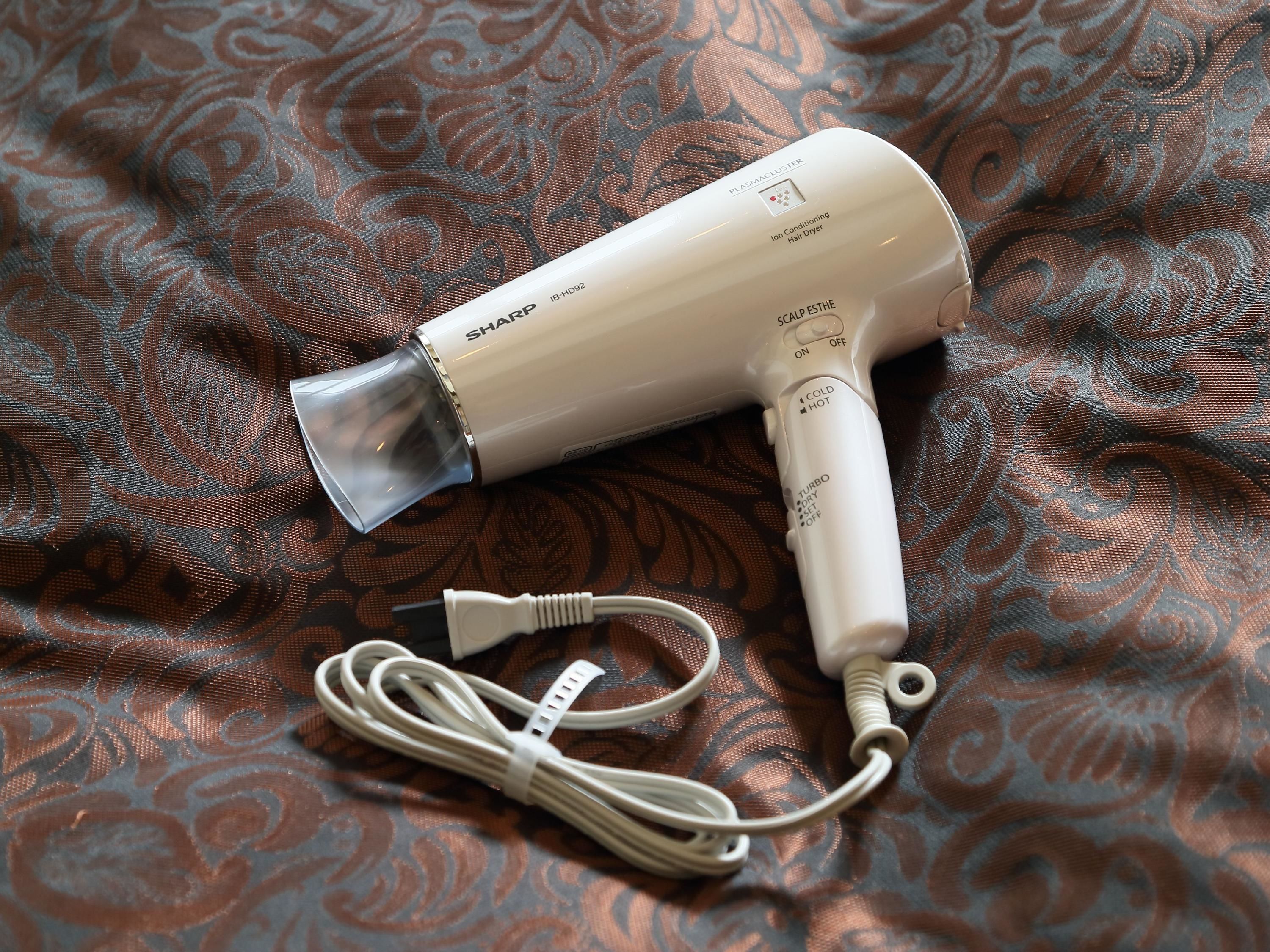 A hair dryer with a cord and a plug on a patterned fabric surface.