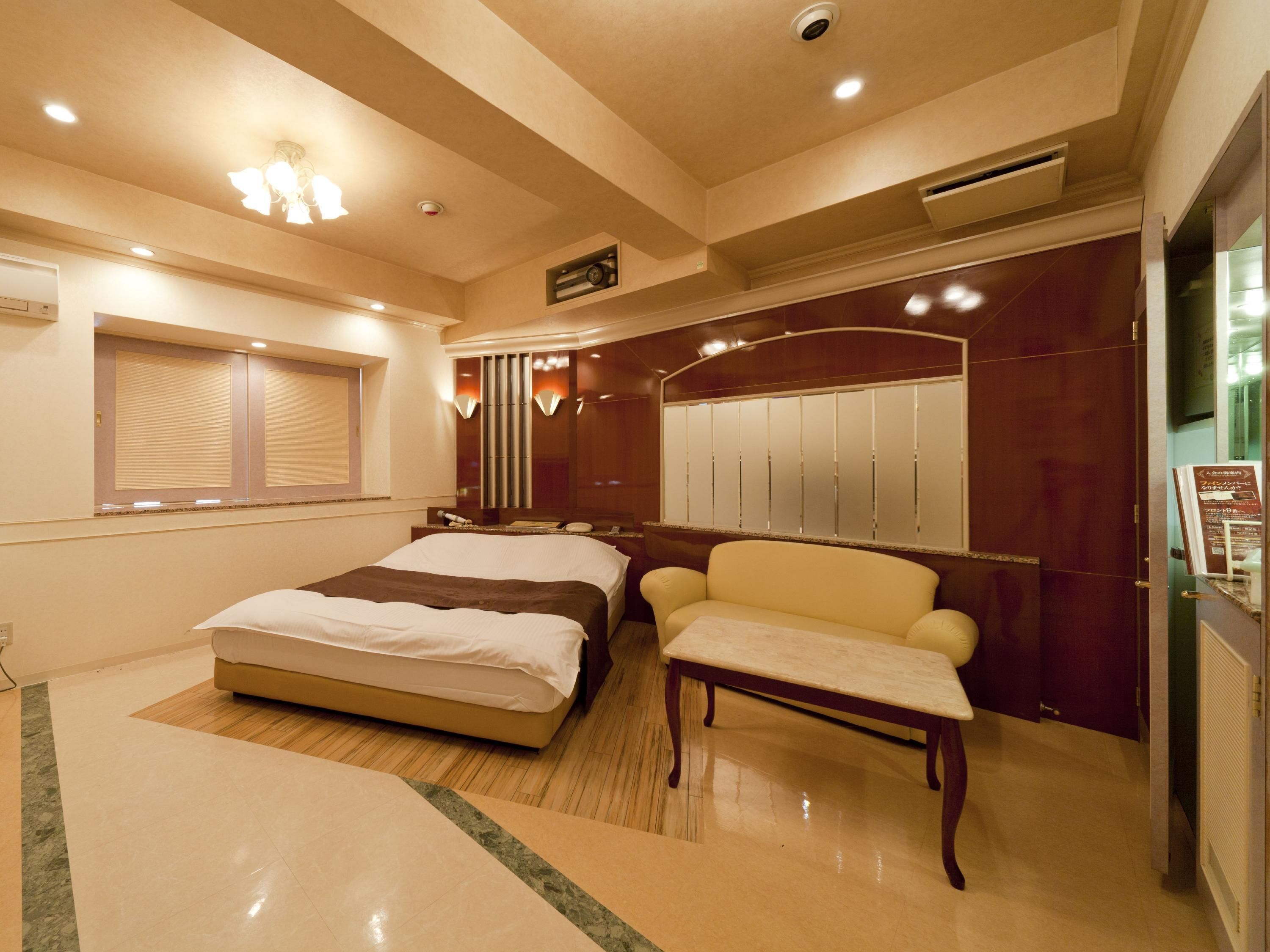 A hotel room with a bed, a chair, a vanity with a mirror, and a wardrobe.