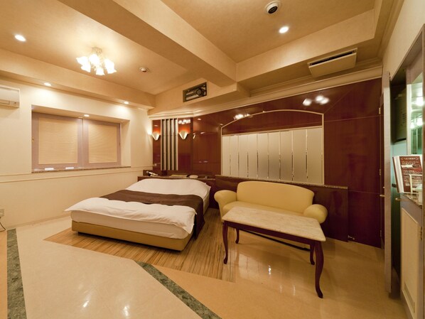 A hotel room with a bed, a chair, a vanity with a mirror, and a wardrobe.