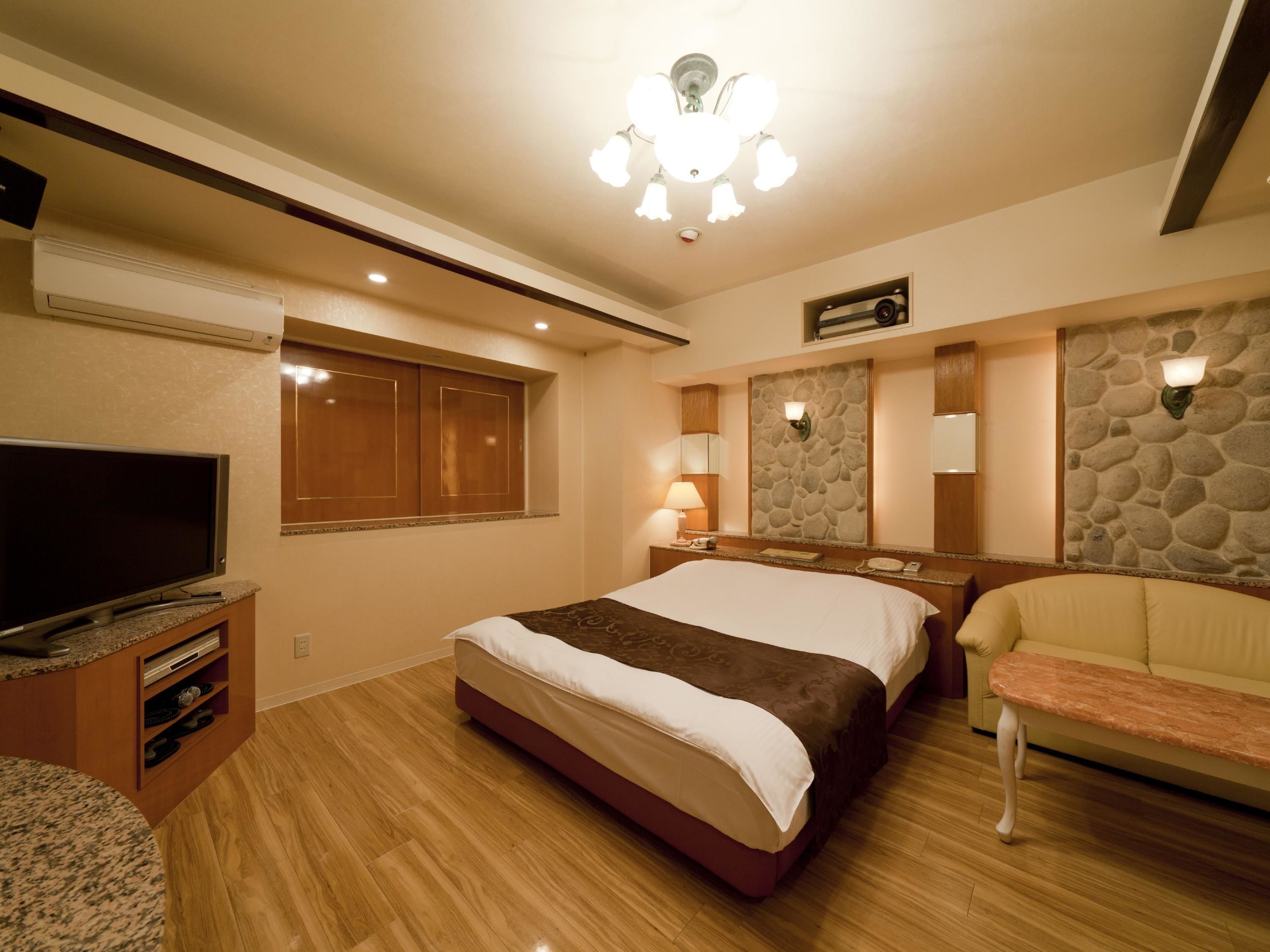 A hotel room with a bed, a TV, a stone wall, and a stone fireplace.