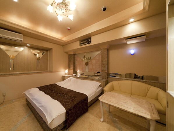 Habitación de hotel con cama, mesita de noche, sofá, espejo y candelabro.