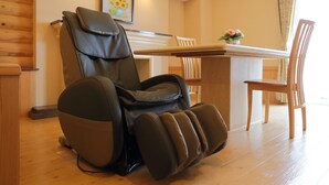 A massage chair in a room with wooden flooring, a dining table with chairs, and a framed picture on the wall.