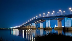 A nighttime view of a bridge with multiple light fixtures and pillars, reflecting on the water below.
