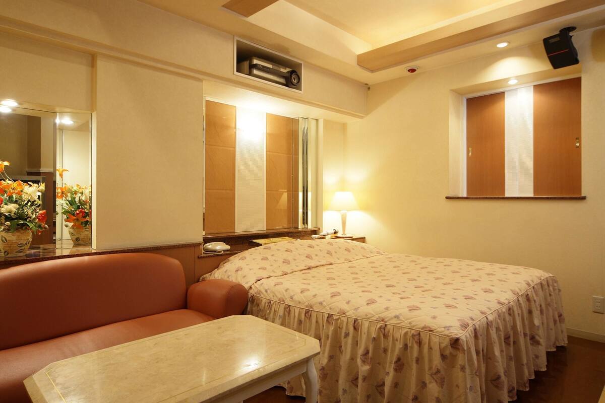 Habitación de hotel con cama, una mesita, un sofá, un espejo, una ventana y un aire acondicionado instalado en la pared.