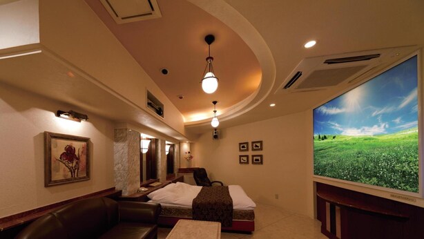 A hotel room with a large TV, a sofa, a bed, and a small table.