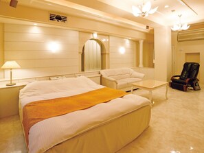 A hotel room with a large bed, a small table, a chair, a massage chair, and a mirror on the wall. - Fine Garden Juso (Osaka)