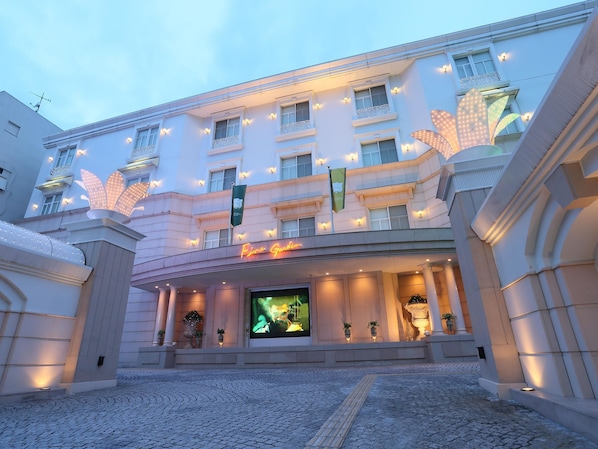 L’entrée d’un hôtel, avec une grande enseigne lumineuse, de nombreuses fenêtres dotées de luminaires et une cour dallée.
