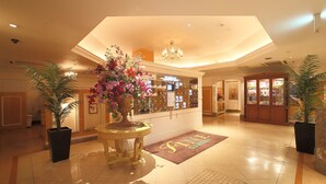 A hotel lobby with a central reception desk, a chandelier, potted plants, and a 'Still Garden' sign. - Hotel Fine Garden Kyoto Minami (Kyoto)