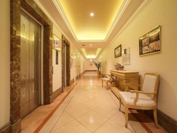 Un pasillo de hotel con ascensores, una recepción y una silla.