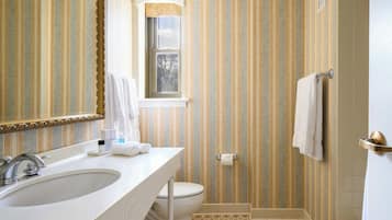 Un baño con papel tapiz a rayas, un espejo grande, un lavabo, un inodoro y una zona de ducha.