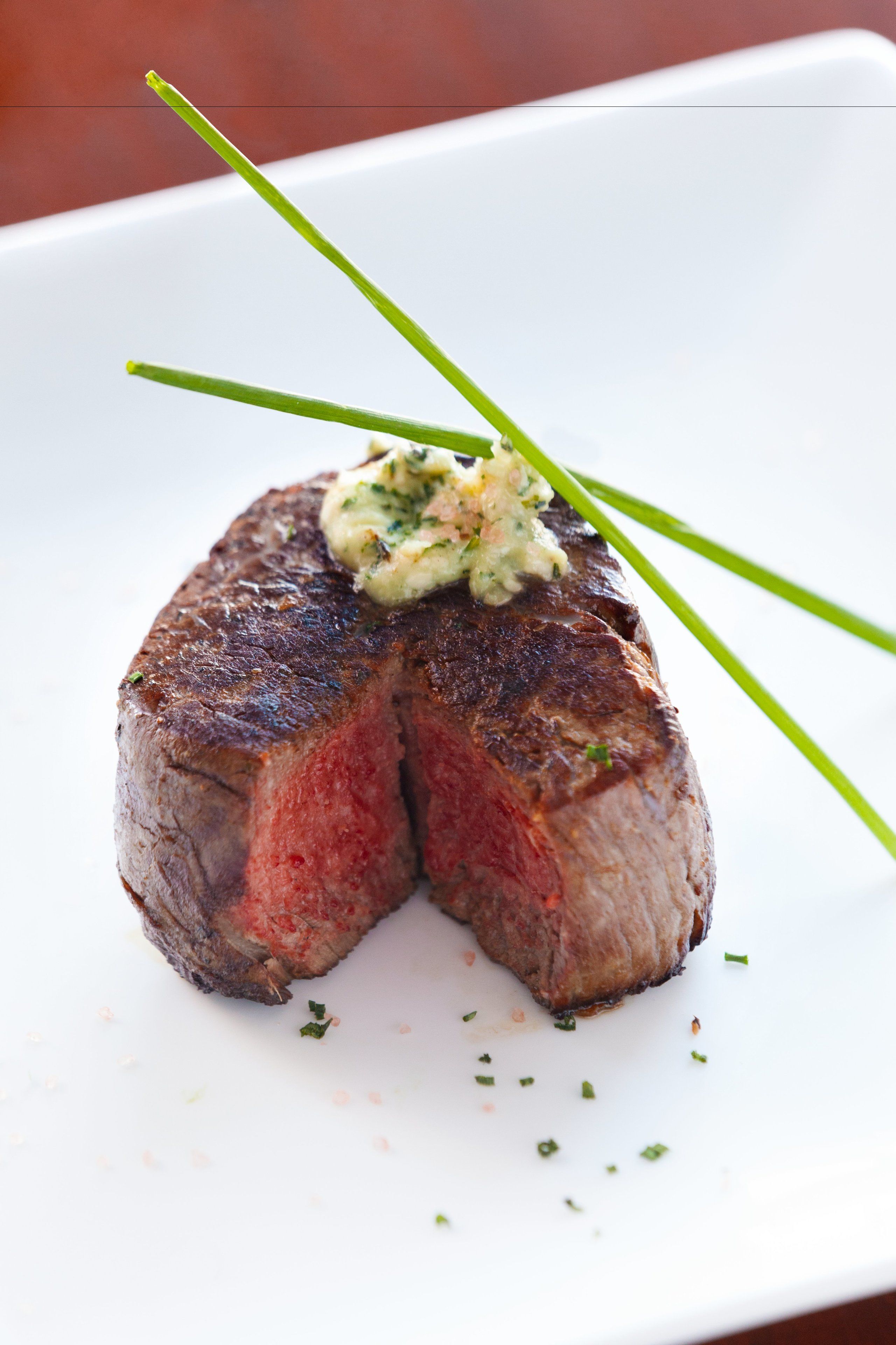 A steak with a side of sauce and garnish on a white plate.