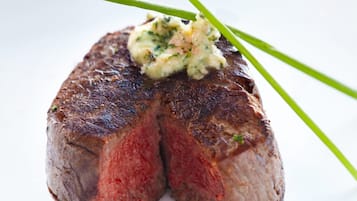 A steak with a side of sauce and garnish on a white plate.
