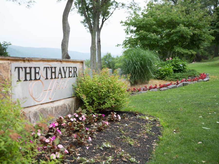 Letrero de 'The Thayer Hotel' con un jardín ajardinado al frente.