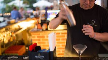 Un cantinero prepara una bebida en la barra, con un fondo de pared de ladrillo y una botella de Martini.