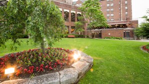 Un patio con un edificio de ladrillo, un árbol y macizos de flores.