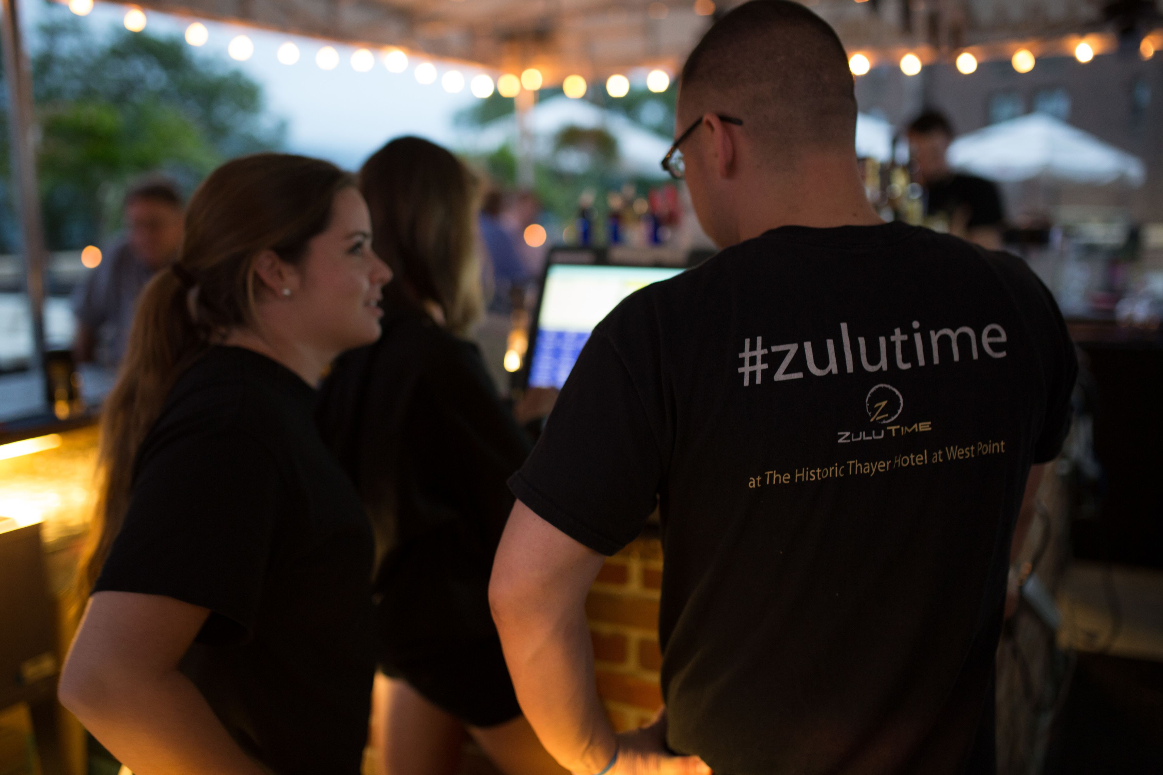 Una persona con camiseta negra que tiene el texto '#zulutime' y 'en The Historic Thayer Hotel en West Point'.