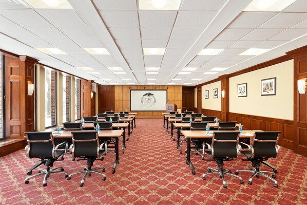 A conference room with a red patterned carpet, wooden panel walls, and a large screen at the front.