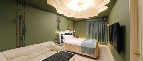 A modern bedroom with a curved ceiling, a bed with a blue blanket, a white sofa, and a flat-screen TV mounted on the wall.