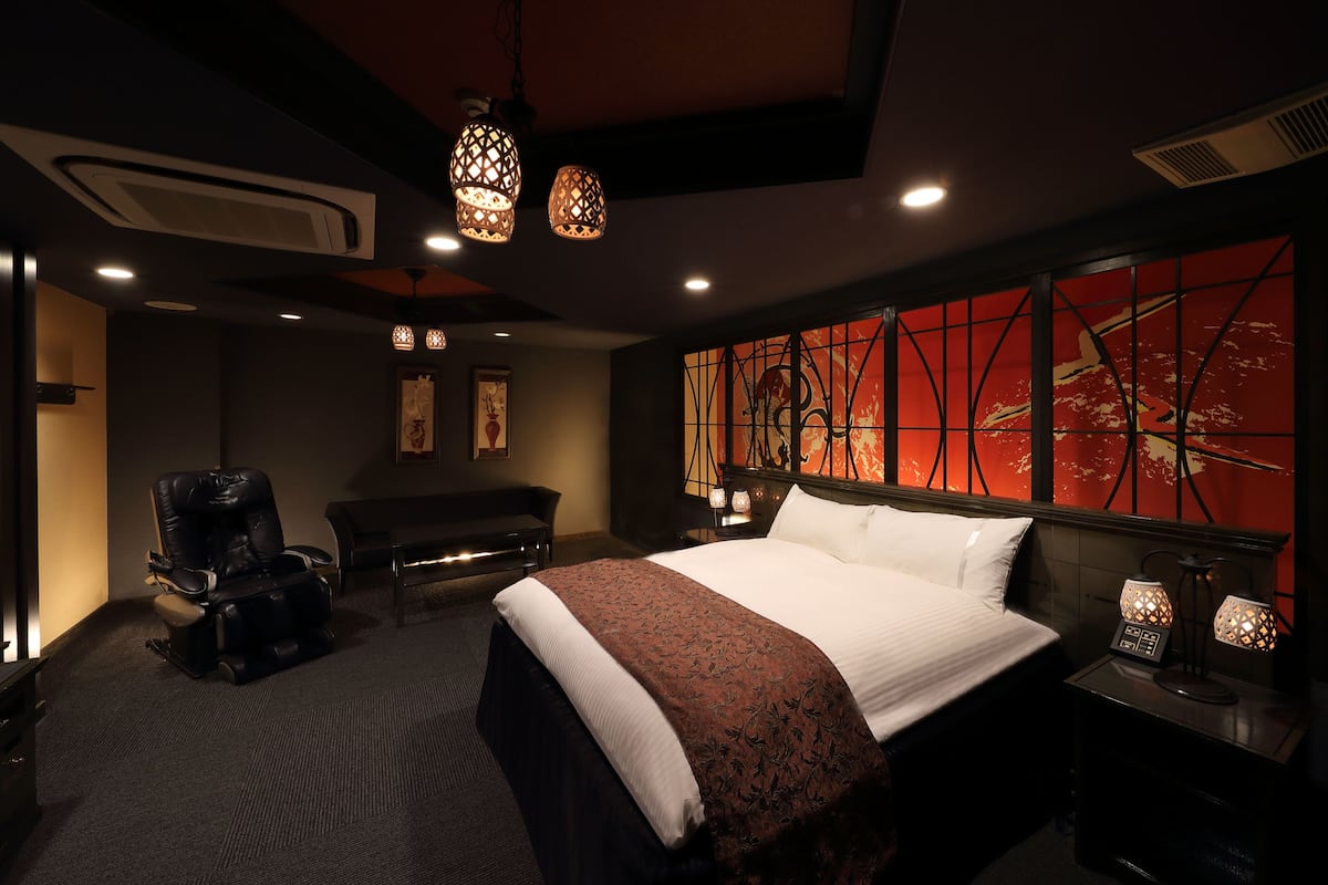Une chambre d’hôtel avec un grand lit, un fauteuil massant, un bureau et un mur orné d’un motif abstrait rouge.