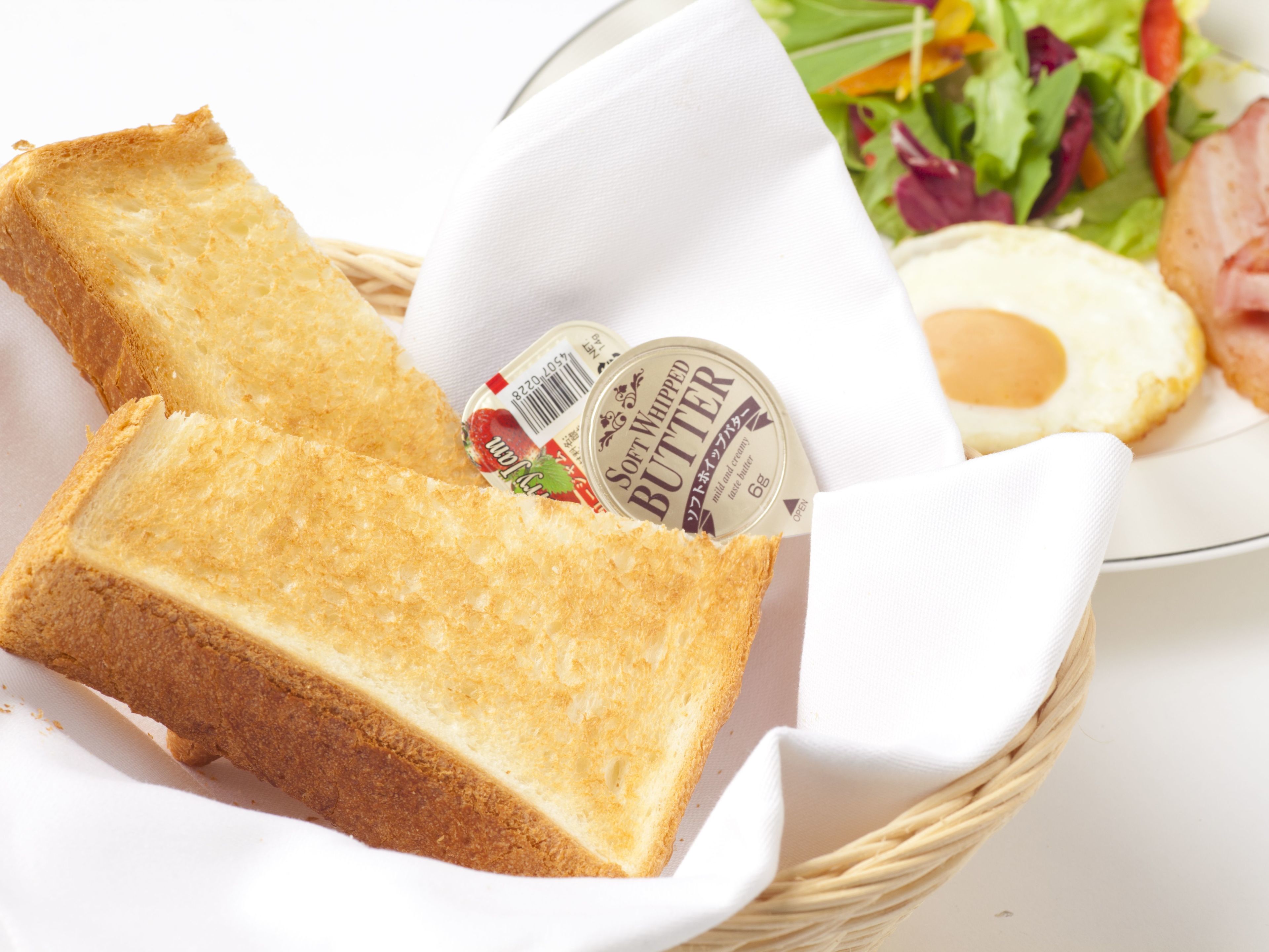 Una cesta con una rebanada de pan tostado, un recipiente con mantequilla batida, un plato con un huevo frito y una ensalada como acompañamiento.
