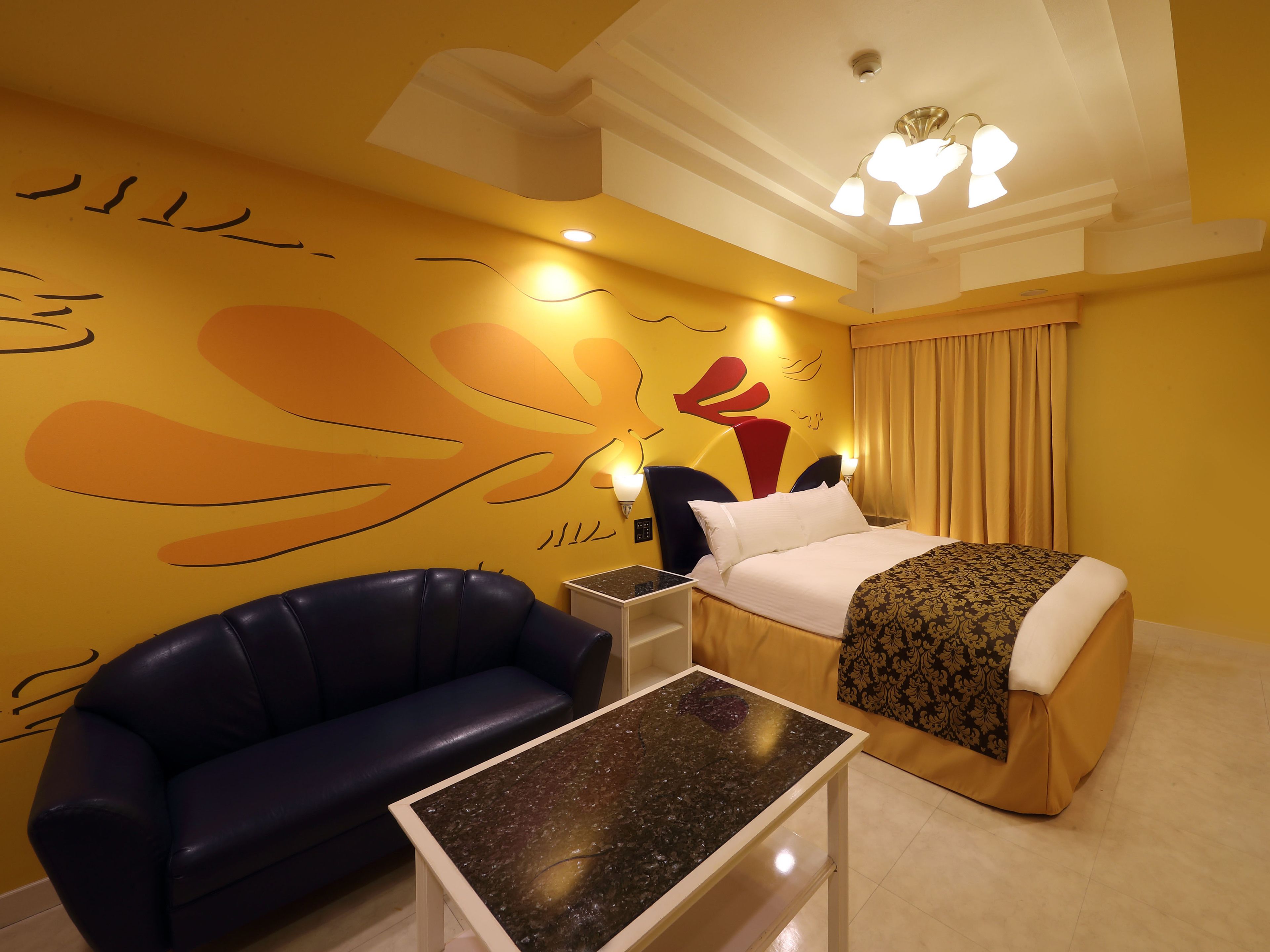 A hotel room with a bed, a blue leather sofa, a small table, and a wall with abstract art.