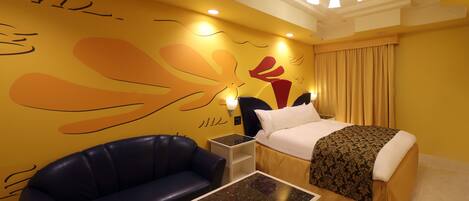 A hotel room with a bed, a blue leather sofa, a small table, and a wall with abstract art.