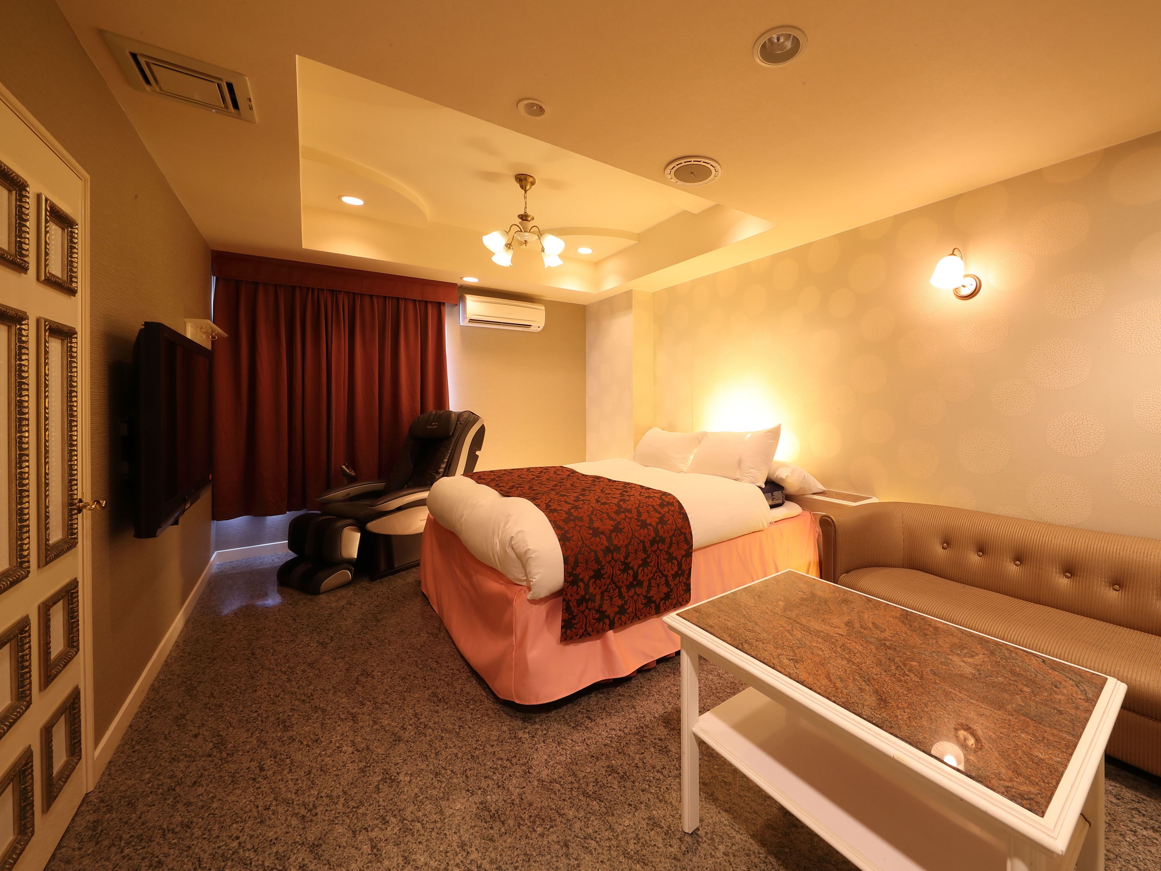 Habitación de hotel con cama, sillón de masajes, televisor, sofá y una mesita de café.