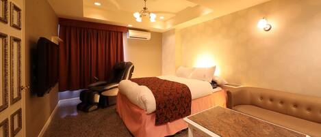 Habitación de hotel con cama, sillón de masajes, televisor, sofá y una mesita de café.