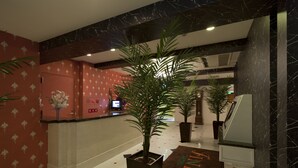 Eine Hotellobby mit einer Rezeption, Zimmerpflanzen und einem Teppich mit dem Namen des Hotels.