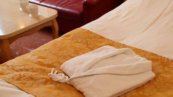 A neatly made bed with a folded white towel, a patterned yellow bedspread, and a red leather chair in the background.