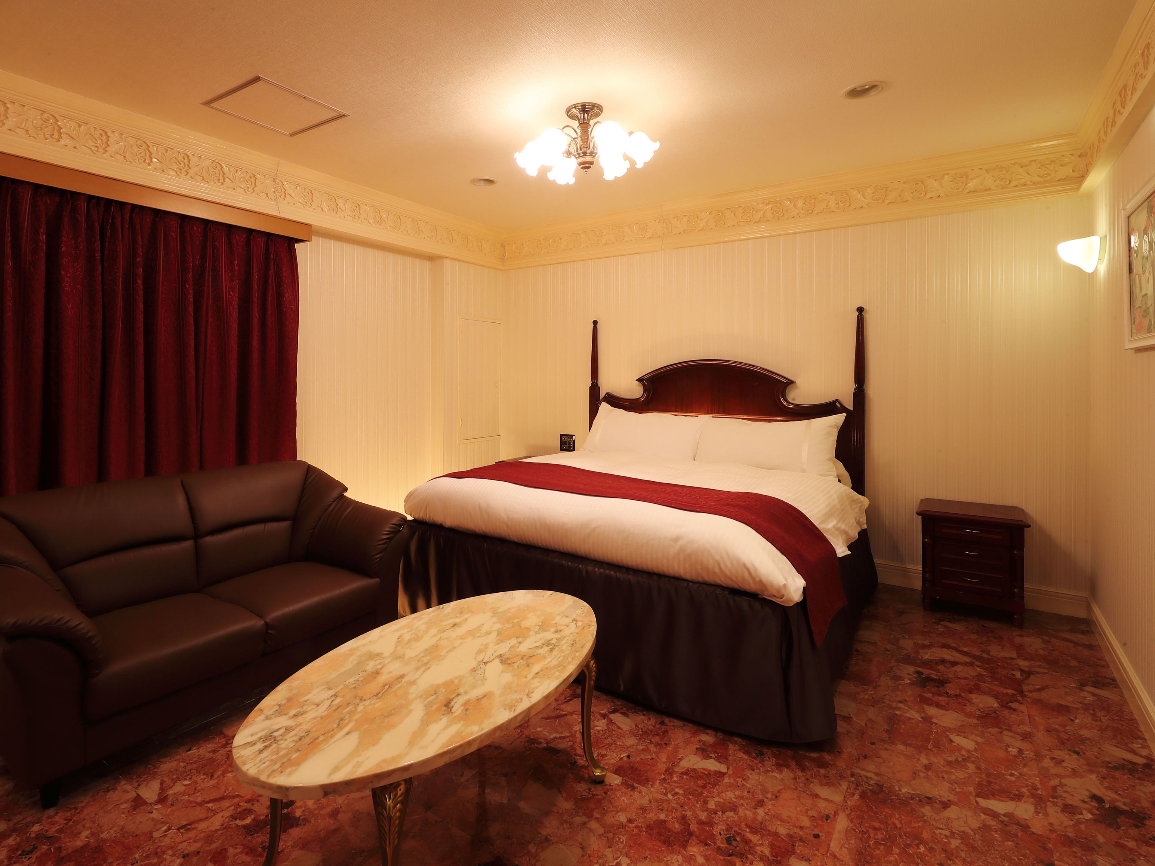 Ein Hotelzimmer mit Himmelbett, Ledersofa, Marmortisch und einem kleinen Nachttisch.