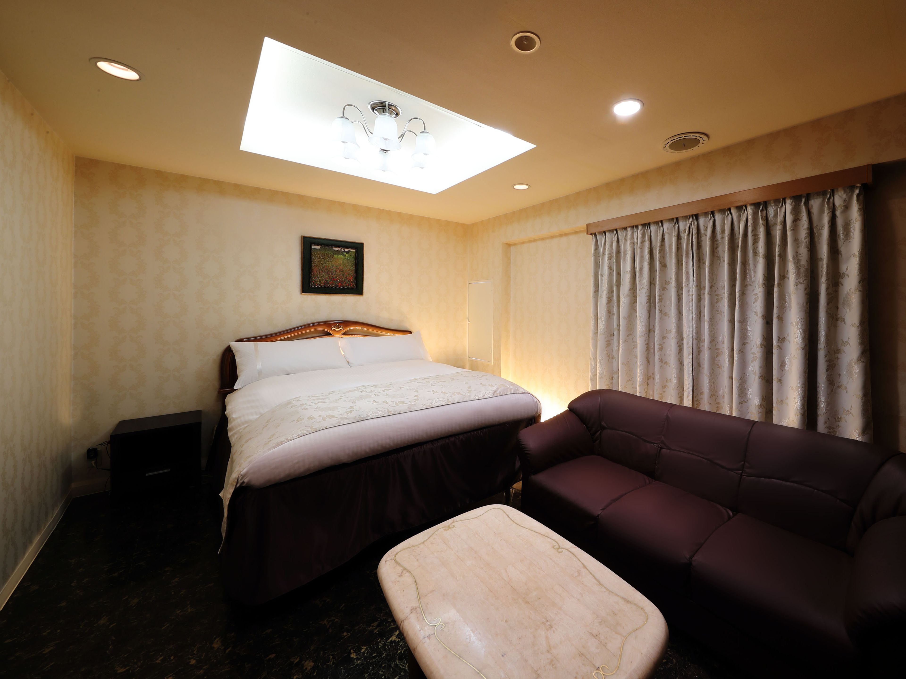 Ein Hotelzimmer mit Bett, Sofa, einem kleinen Tisch, einer Deckenleuchte und einem Fenster mit Vorhängen.