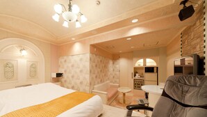 A bedroom with a large bed, a sofa, a small table, and a bathroom visible through an archway.