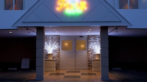 Entrada de hotel con un letrero de neón, pared de ladrillo y diseño moderno.