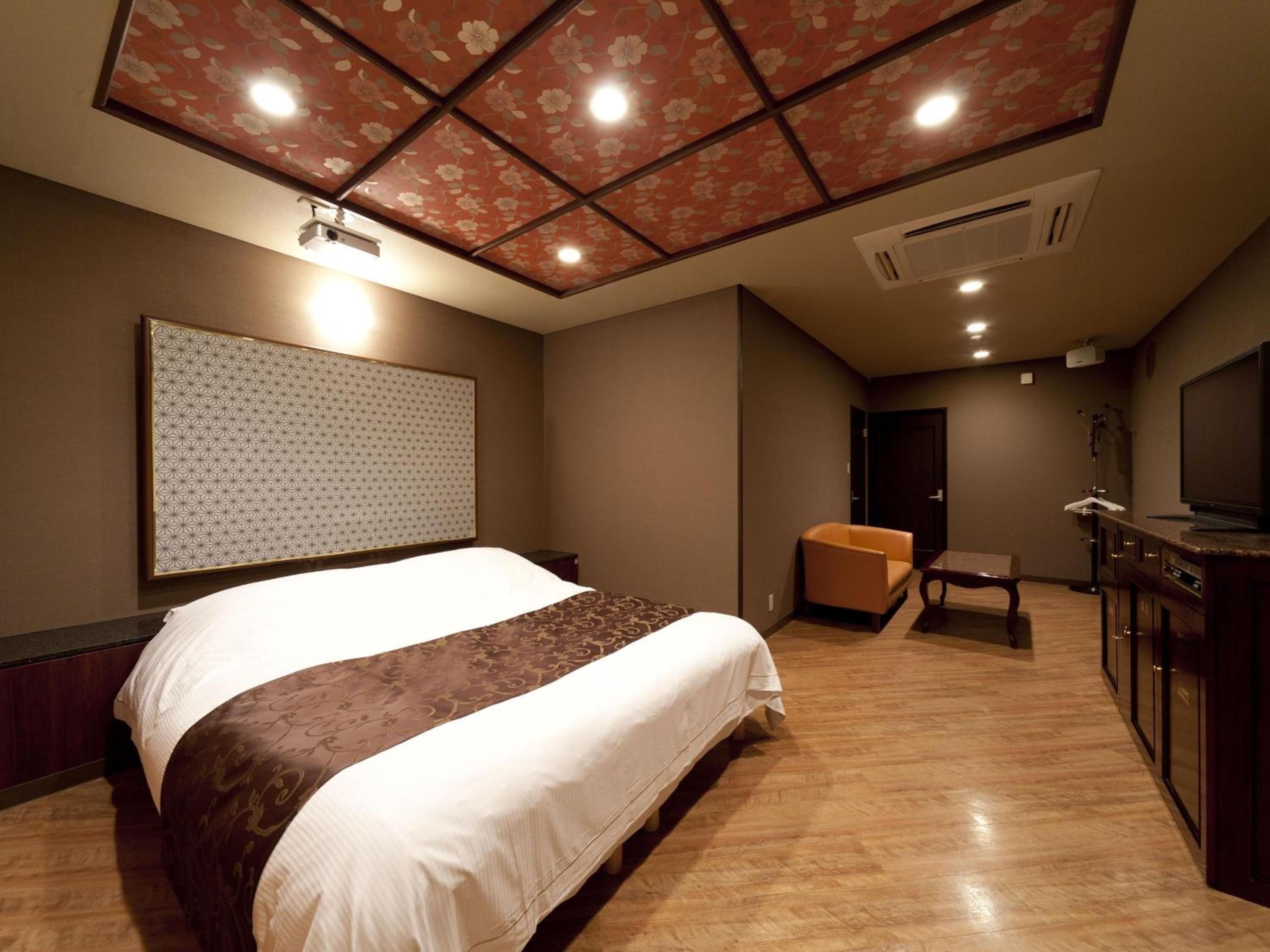 A hotel room with a large bed, a seating area with a sofa and a chair, a television, and a minibar.