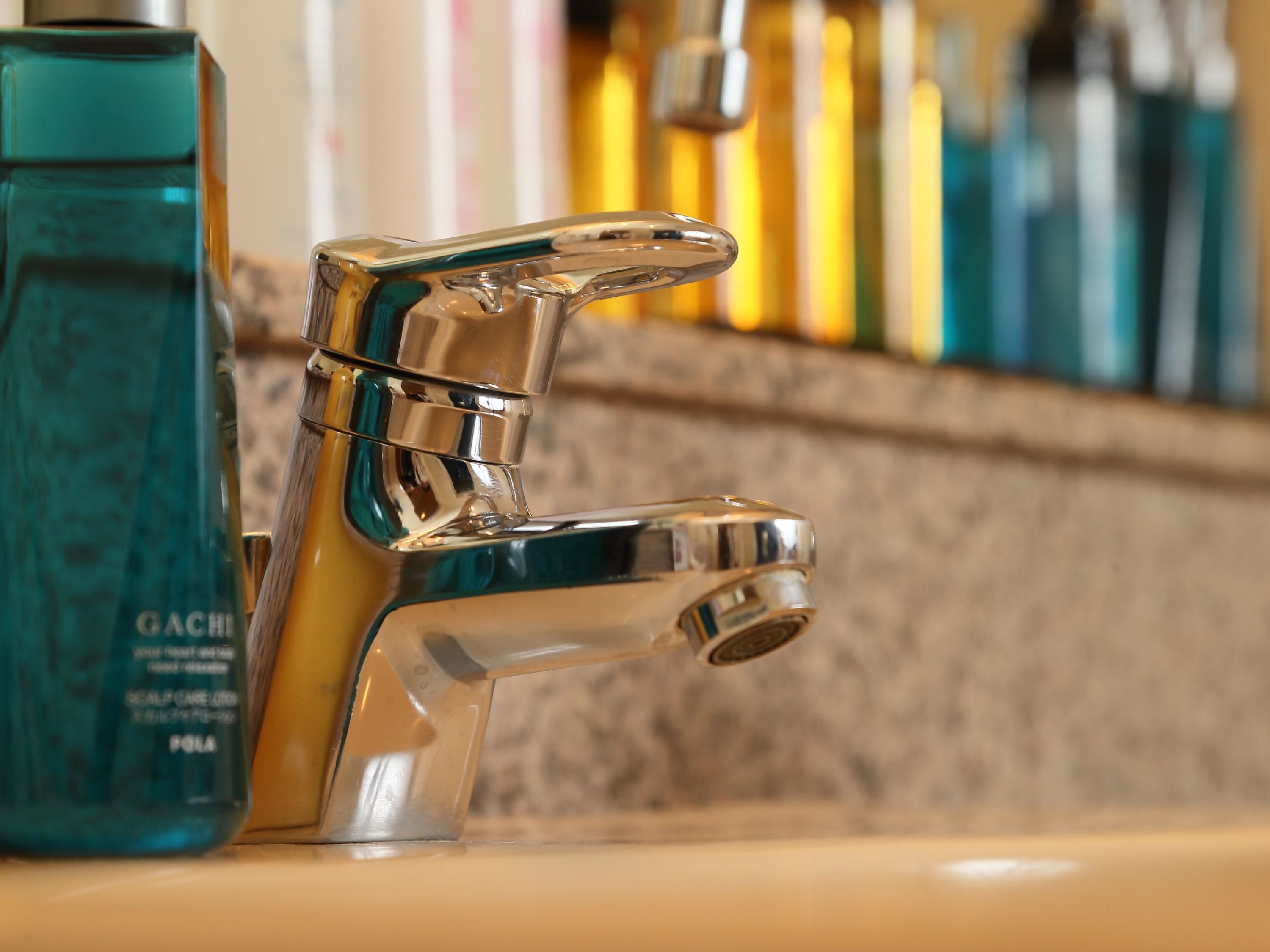 Un grifo cromado de diseño moderno, junto a una botella verde aguamarina del producto capilar GACHIA.