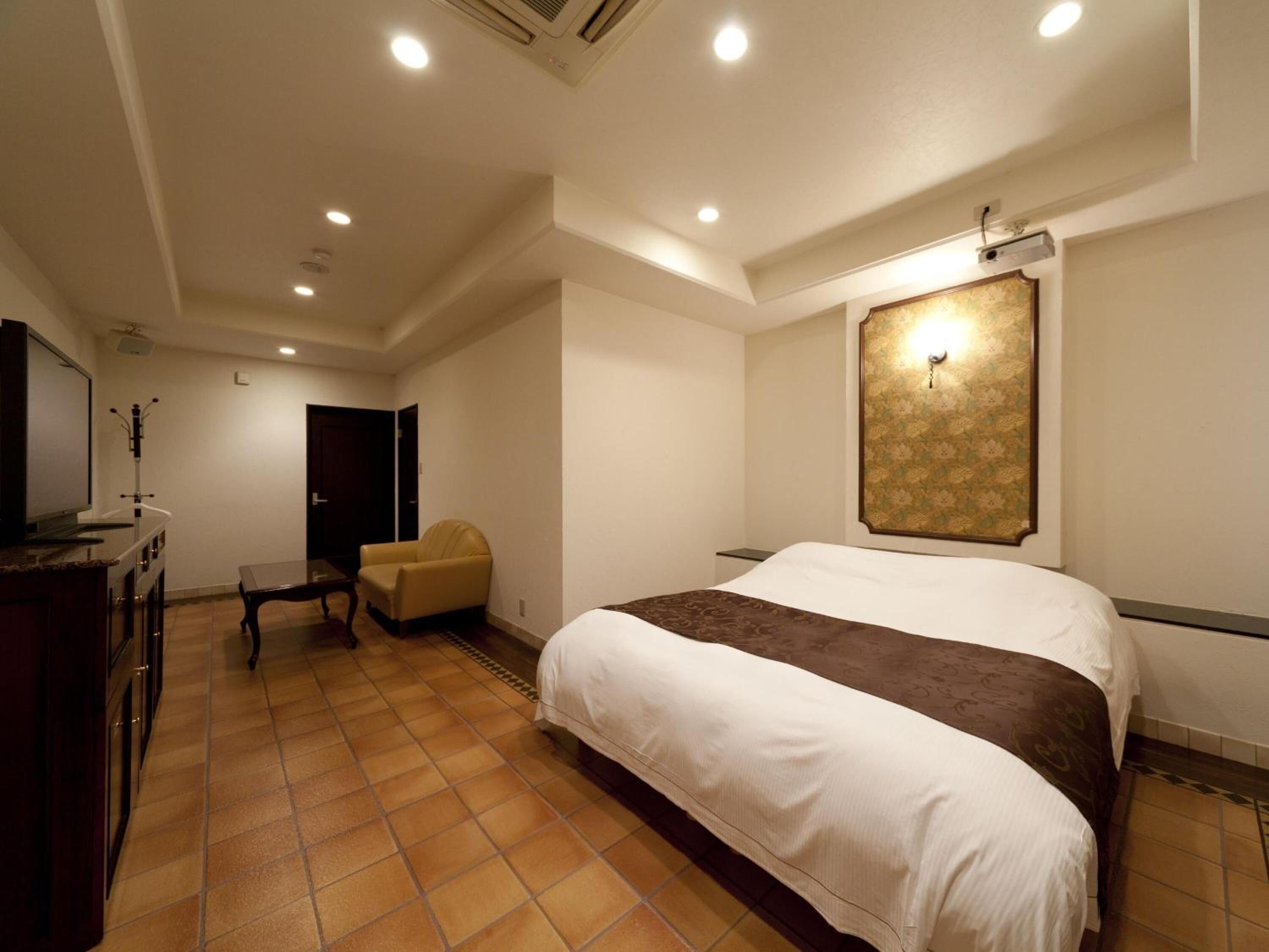 A hotel room with a large bed, a TV, a desk, and a chair.