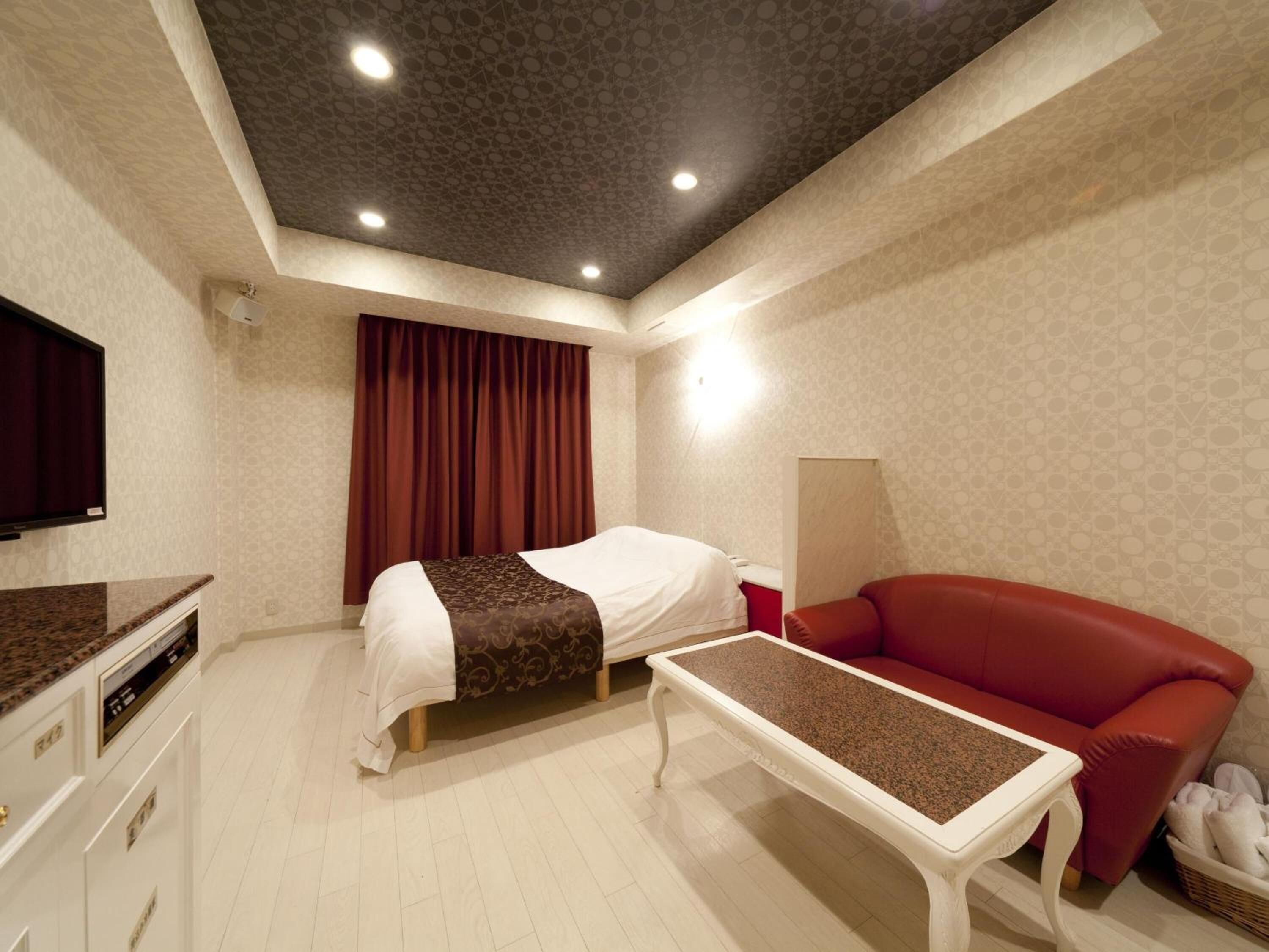 Een hotelkamer met een bed, een rode bank, een klein tafeltje, een televisie en een plafond met inbouwspots.