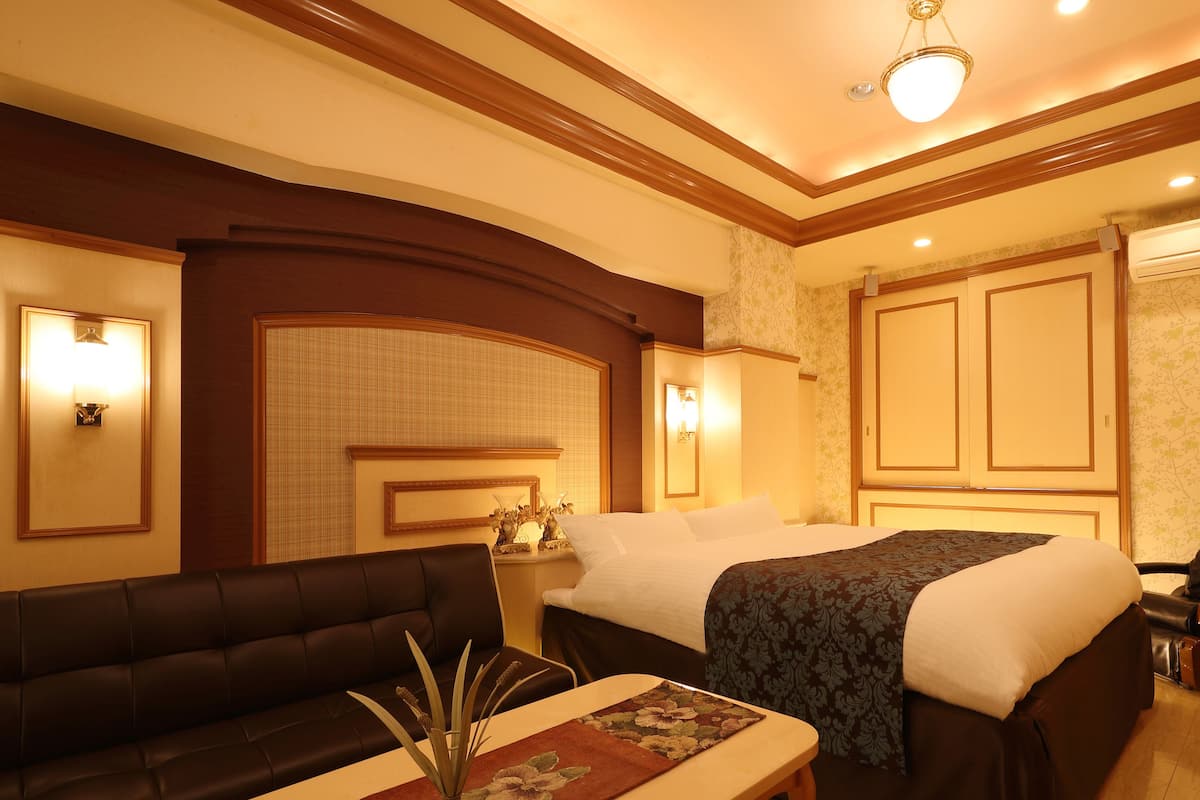 Ein Hotelzimmer mit Sofa, einem Bett mit floralem Überwurf, einem Nachttisch mit Lampe und einer dekorativen Vase.