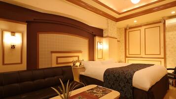 A hotel room with a double bed, a sofa, a small table with a vase, and a decorative mirror.