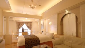 A hotel room with a large bed, a sofa, a wooden coffee table, and a dining area with a table and chairs. - Fine Garden Nara Horai (Nara)