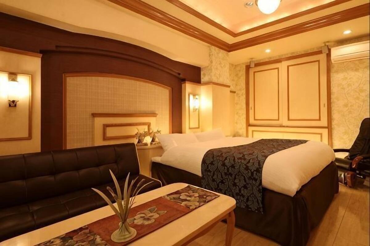 Ein Hotelzimmer mit Bett, Sofa, Nachttisch und einem an der Wand befestigten Fernseher.