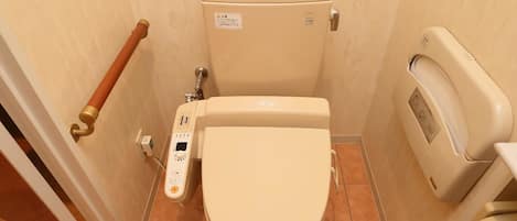 A small, compact bathroom with a toilet, a hand sanitizer dispenser, and a toilet paper holder.