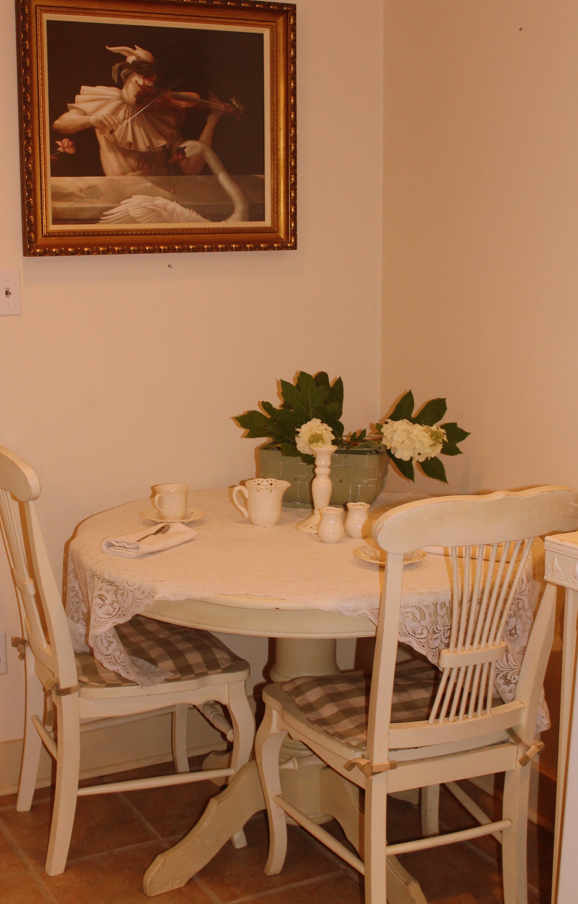 Una mesa de comedor con mantel de encaje, dos sillas y un florero con flores.