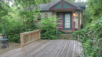 A wooden deck leading to a house with a green roof, surrounded by lush greenery.