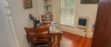 A dining area with a wooden table and chairs, a coffee maker, and a window with blinds.