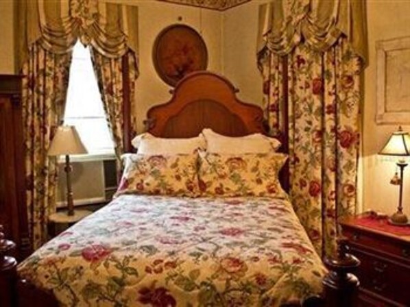A bedroom with a wooden bed, floral bedding, a bedside table, and curtains.