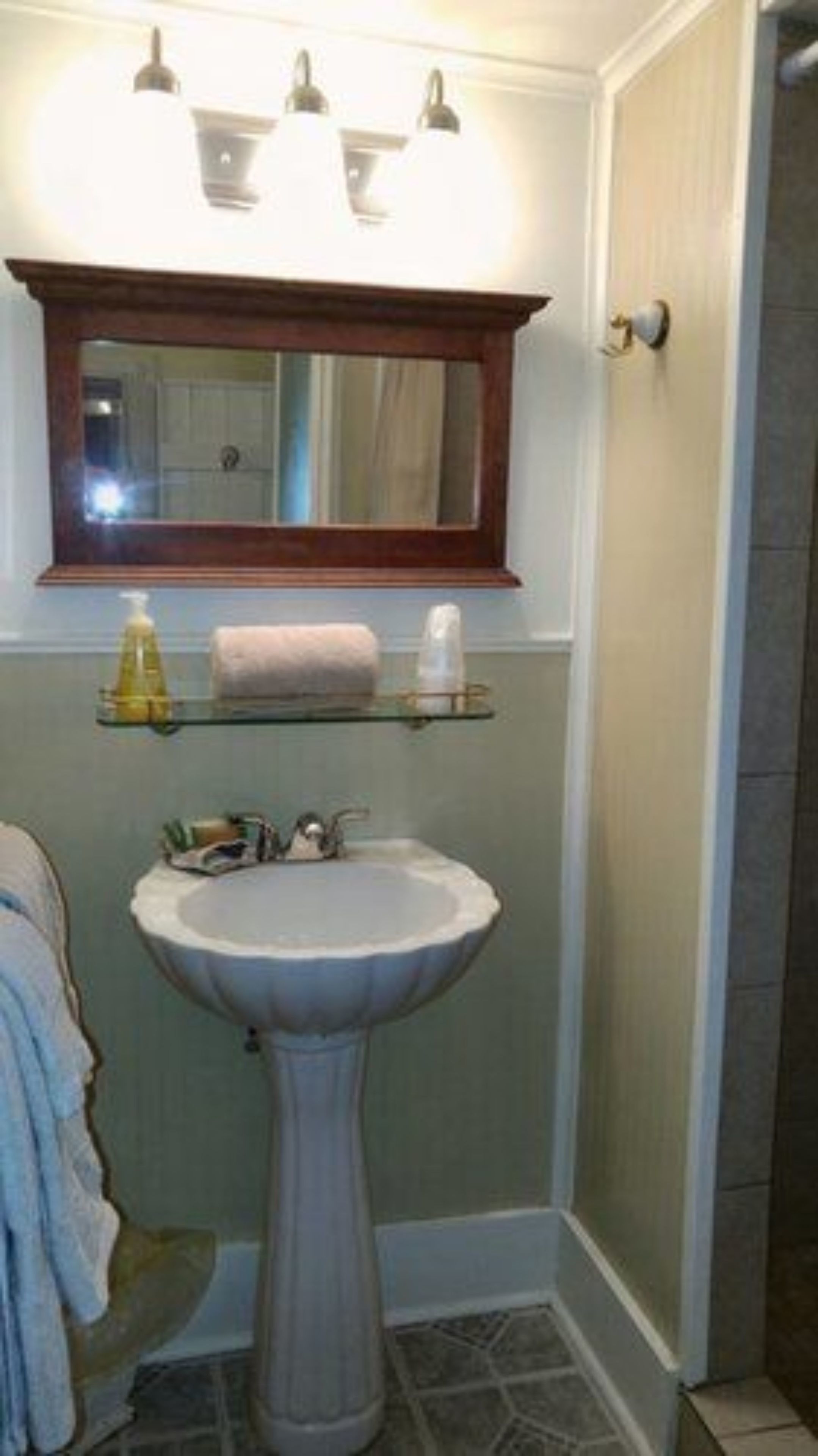 A bathroom with a pedestal sink, a mirror above it, and a shelf with toiletries.