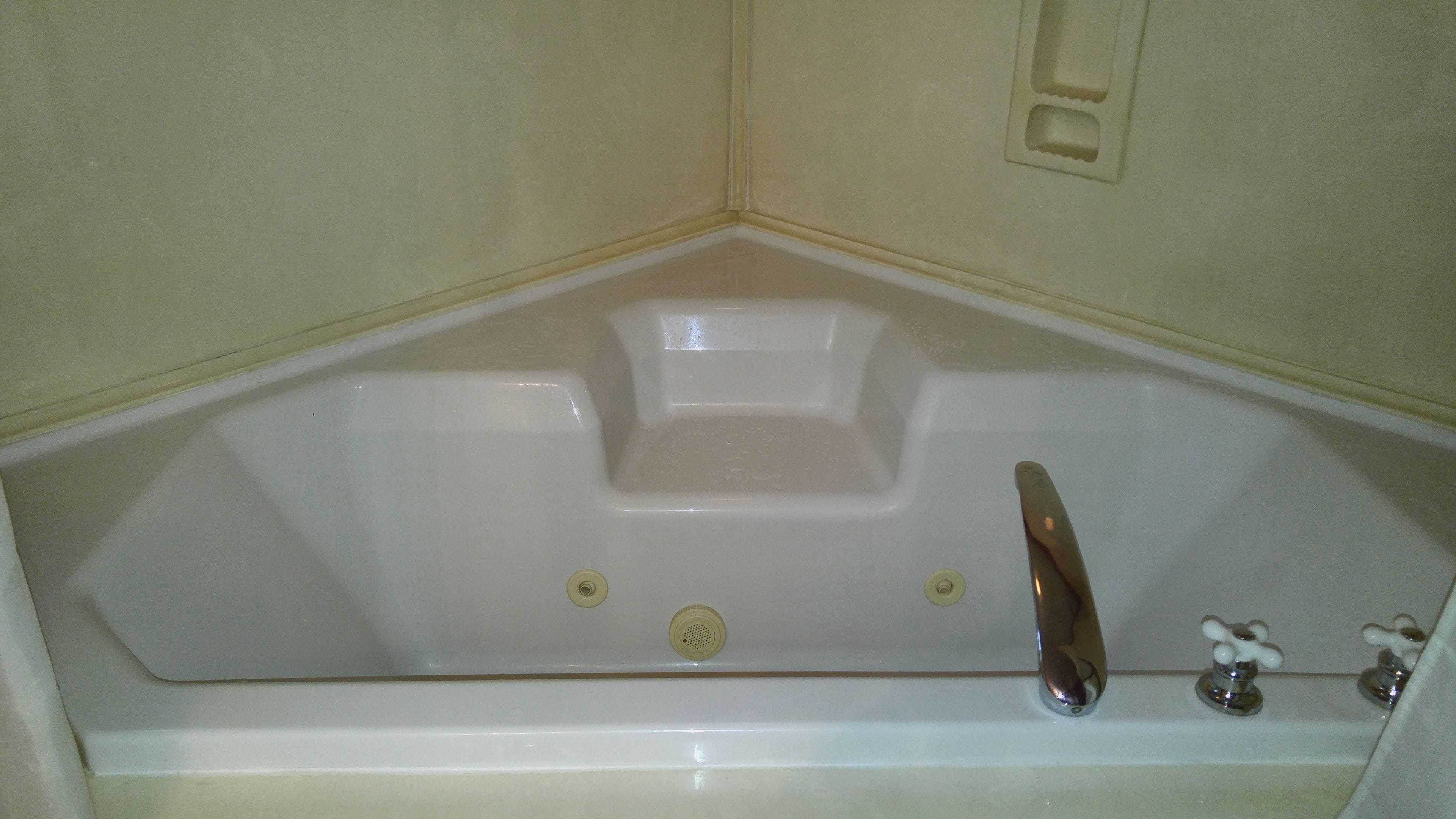 A standard bathtub with a built-in seat, two faucets, and a drain.