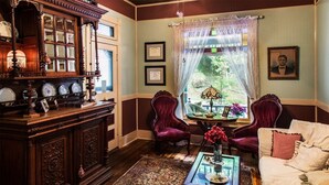 A traditional room with a wooden cabinet, two red velvet chairs, a white sofa, and a patterned rug. - Hidden Springs Bed & Breakfast (Eureka Springs)